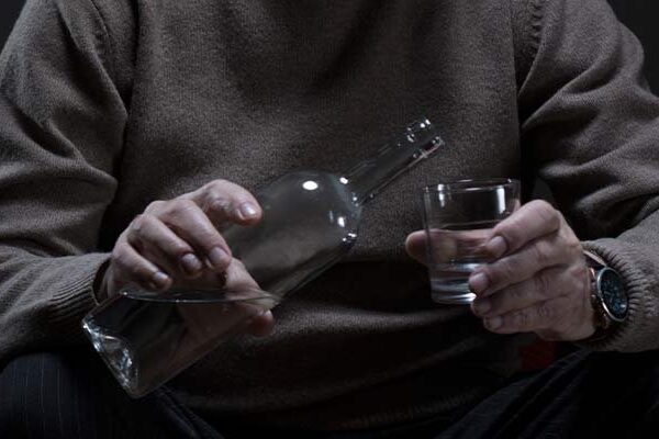 Person wearing a sweater pouring liquid into a glass.