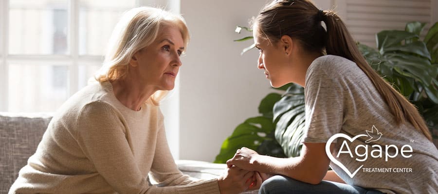 Person in beige sweater looking at woman holding hands.