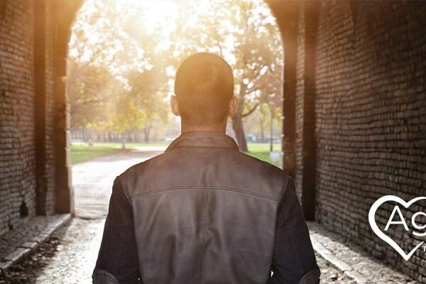 Person in a black jacket walking through a sunlit tunnel with Agape Treatment Center logo.