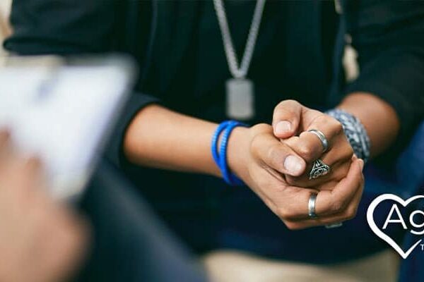 Person wearing rings and bracelets sitting with hands clasped.