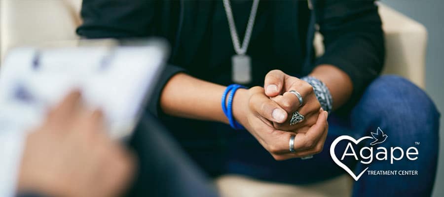 Person wearing rings and bracelets sitting with hands clasped.