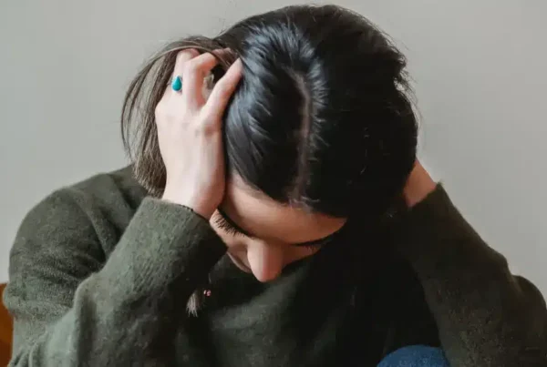 Person with dark hair in green sweater holding head in hands.