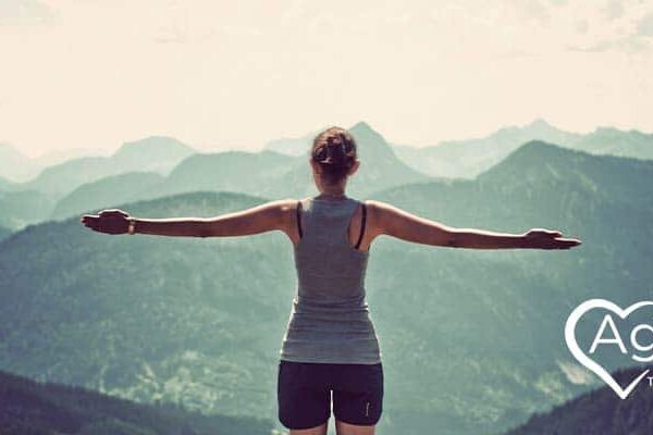 Person in athletic wear with arms outstretched overlooking mountains.