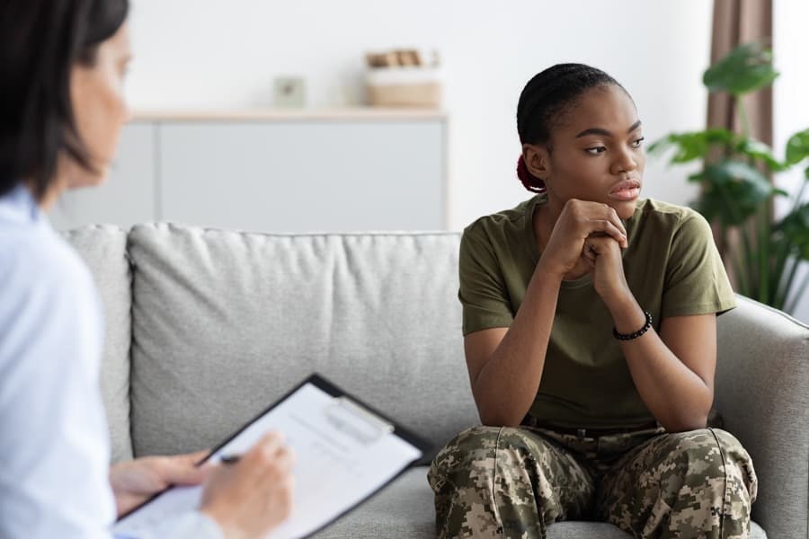 Portrait of black soldier woman having meeting with psychologist, african american female in military uniform sitting on the couch during therapy session, suffering depression, selective focus