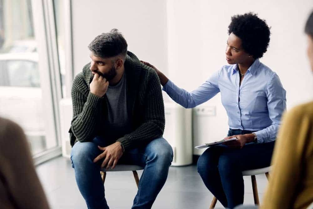 woman in group therapy supporting sad man