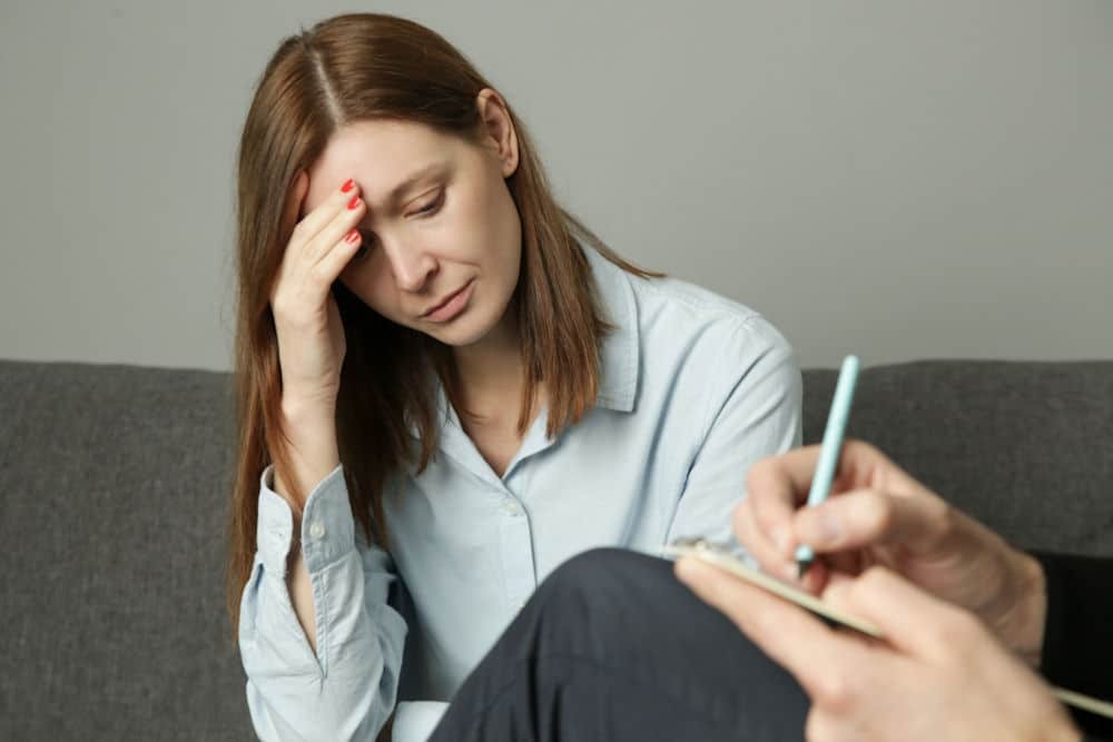 anxious woman touching her forehead as therapist takes notes