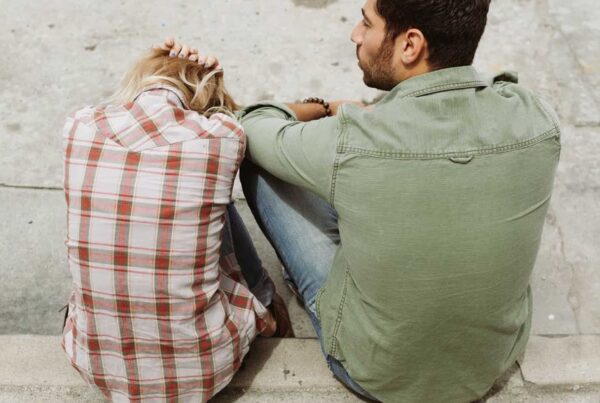man and woman sitting together by a street while the woman has her head down