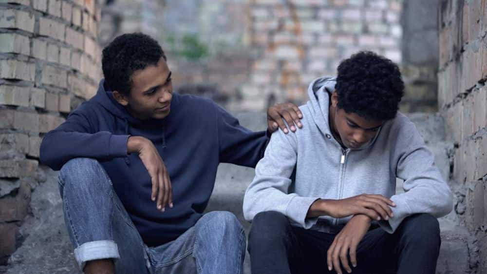 two young men sitting together outside one feeling sad