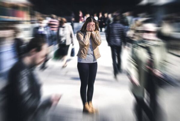 Woman in a crowded space with her hands covering her face and people around her are blurred