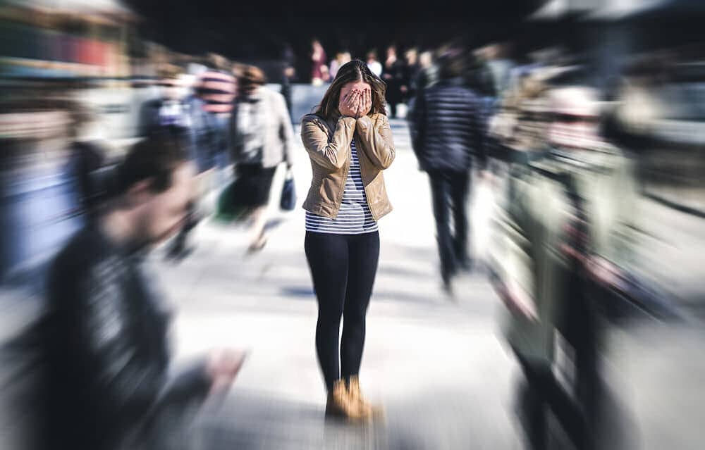 Woman in a crowded space with her hands covering her face and people around her are blurred