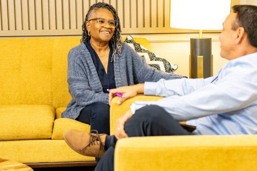 Person wearing a blue cardigan conversing on a yellow sofa.