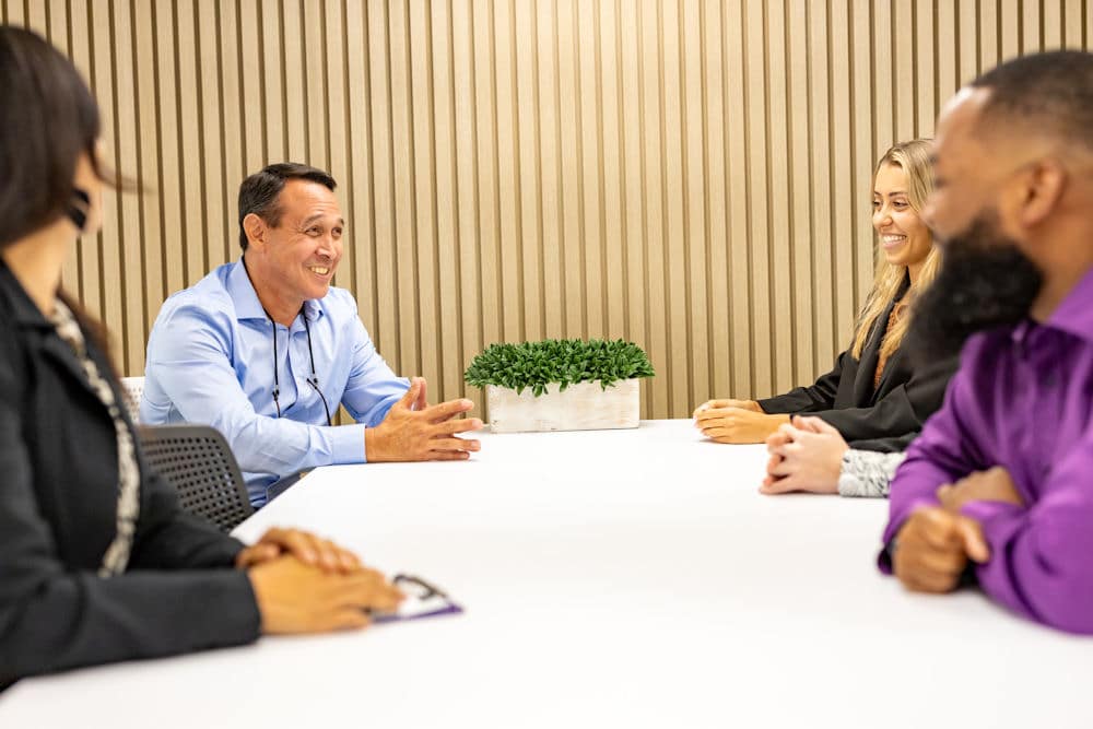 Person in blue shirt speaking at a meeting table.