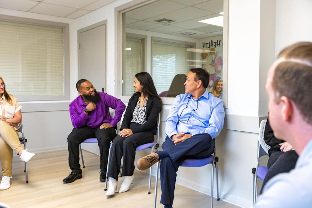 People sitting in a circle, engaged in conversation, wearing business casual clothing.