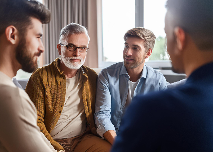 Men sitting together, one with a brown cardigan and glasses.