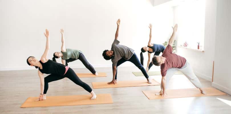 People practicing yoga poses on orange mats in a bright studio.