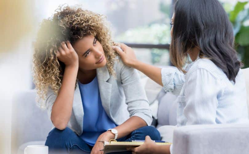 Person in gray blazer comforting another in striped shirt.