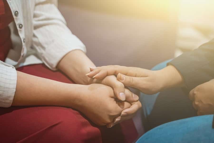 Two people holding hands in comfort, wearing long sleeves.