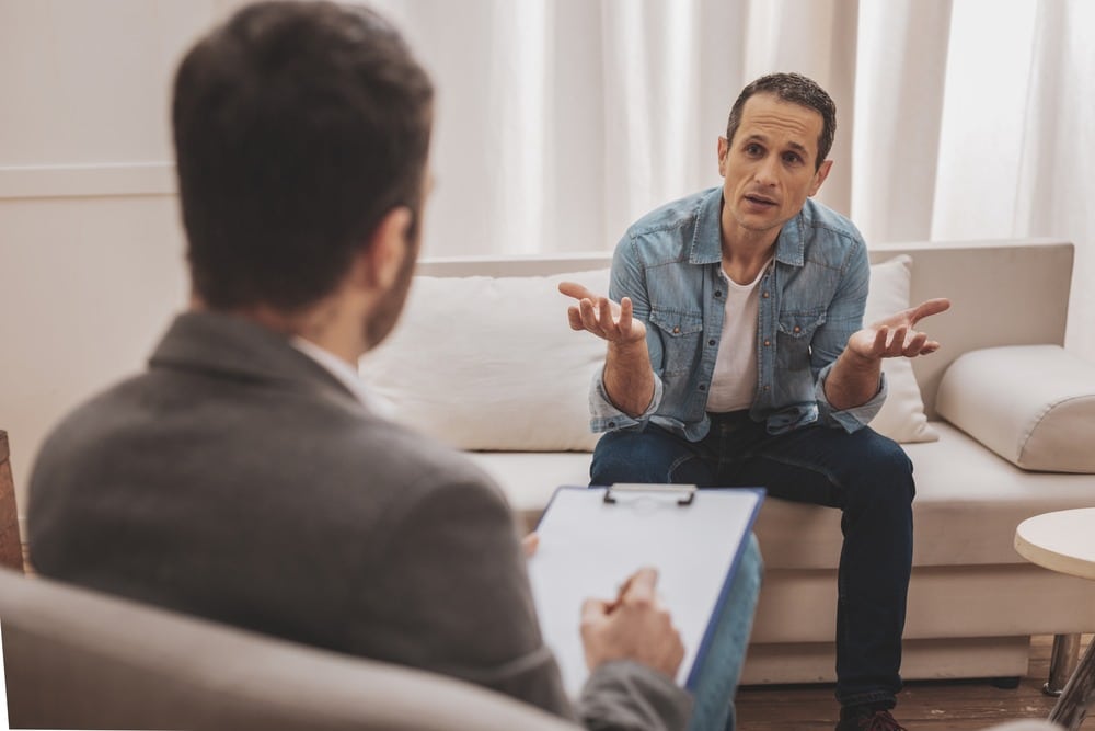 Person in denim jacket sitting on sofa, gesturing with hands.