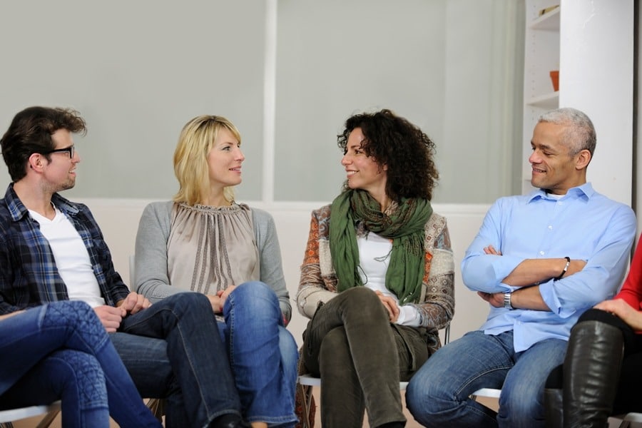 People sitting in a group, wearing casual clothes and engaging in conversation.
