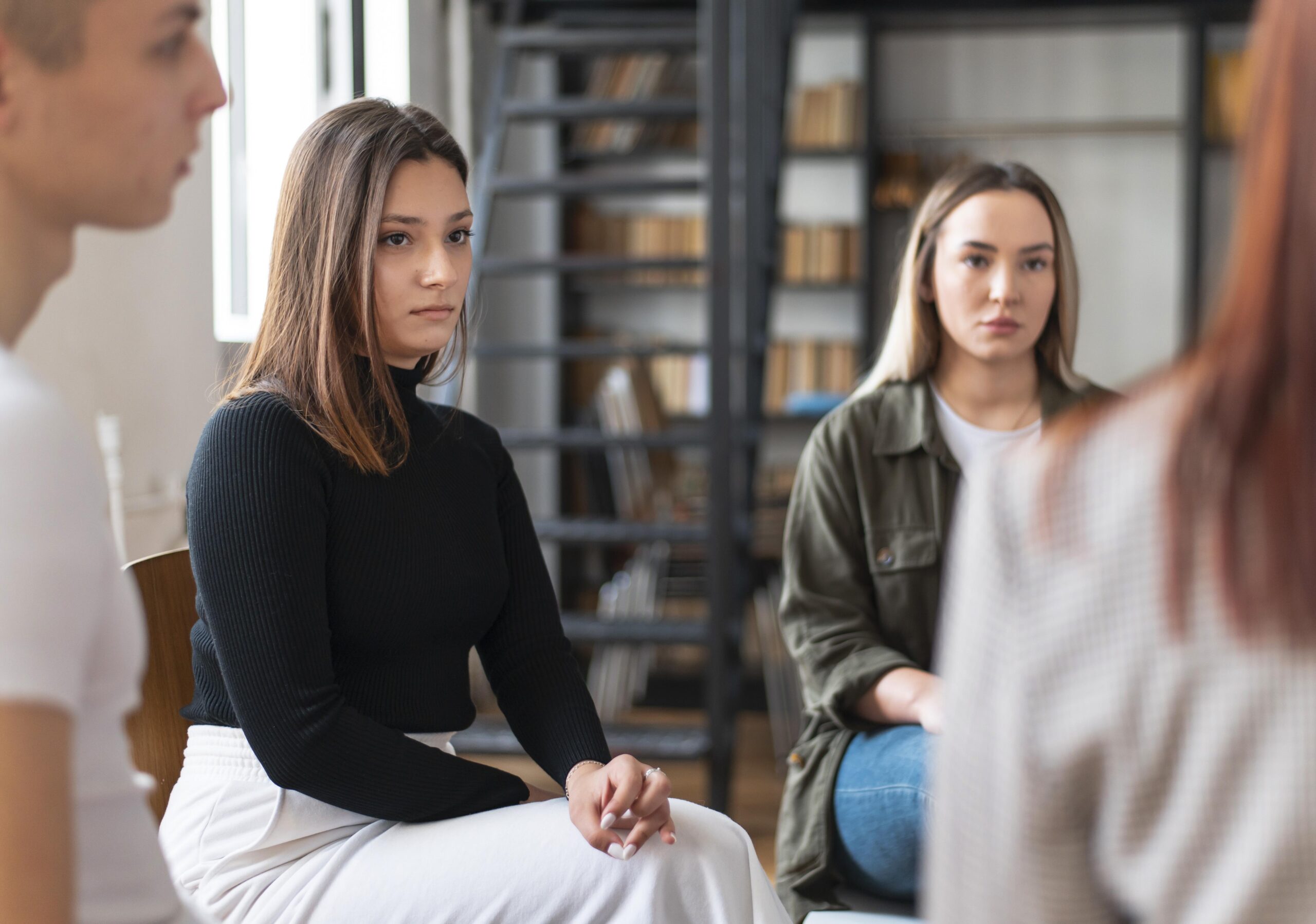 Person in black sweater sitting attentively in a group setting.